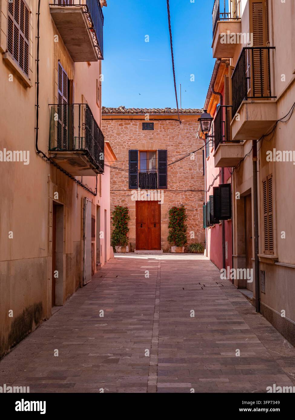 Uno stretto vicolo lastricato si snoda tra tradizionali edifici in pietra mediterranea con persiane in legno nel quartiere storico di Alcudia, mostrando autò Foto Stock