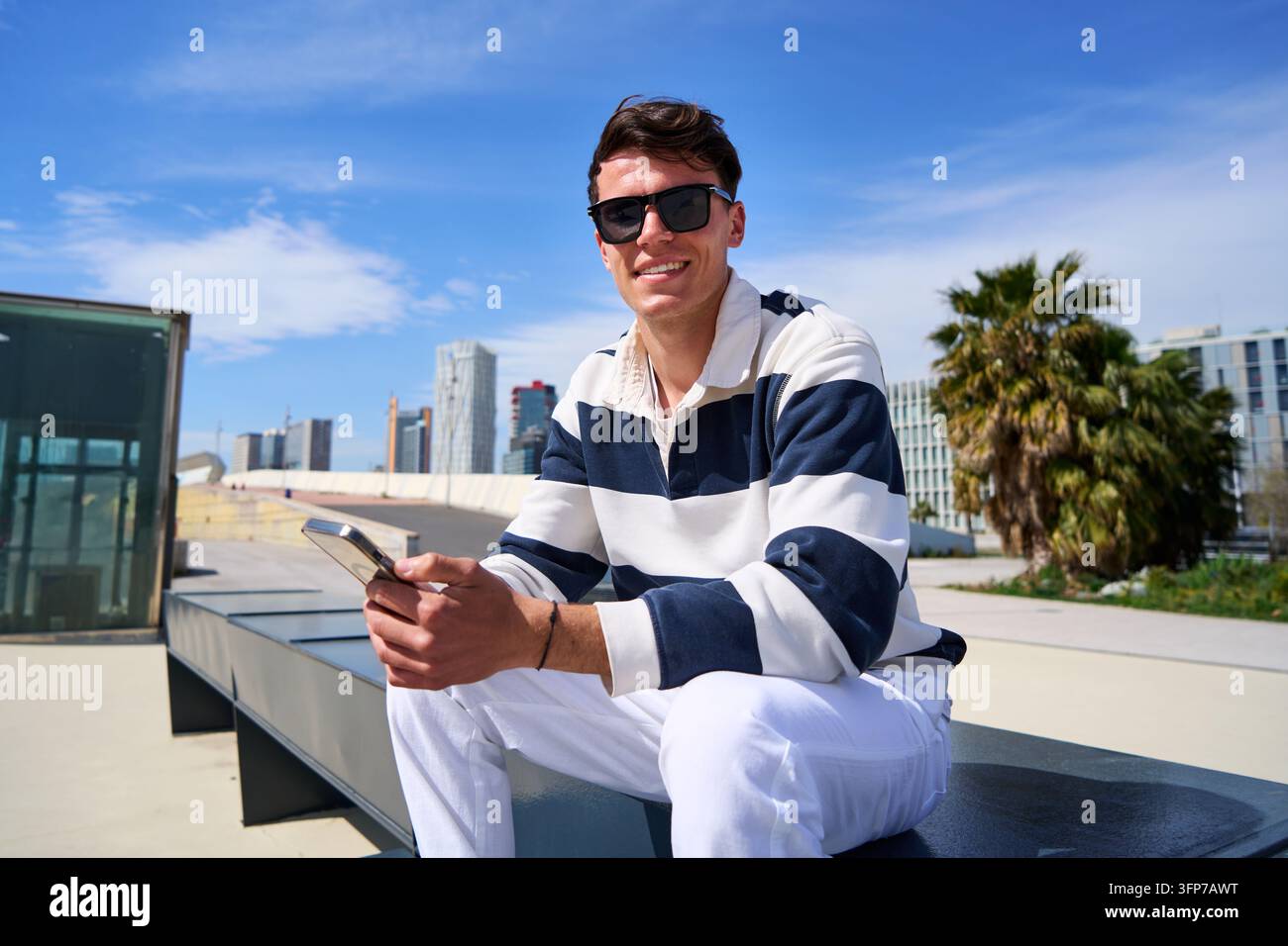 Giovane uomo che sorride mentre usa uno smartphone in un ambiente urbano Foto Stock