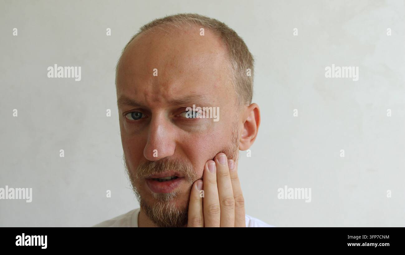Uomo che tocca la guancia soffrendo di forti dolori dentali e problemi di sensibilità dei denti Foto Stock