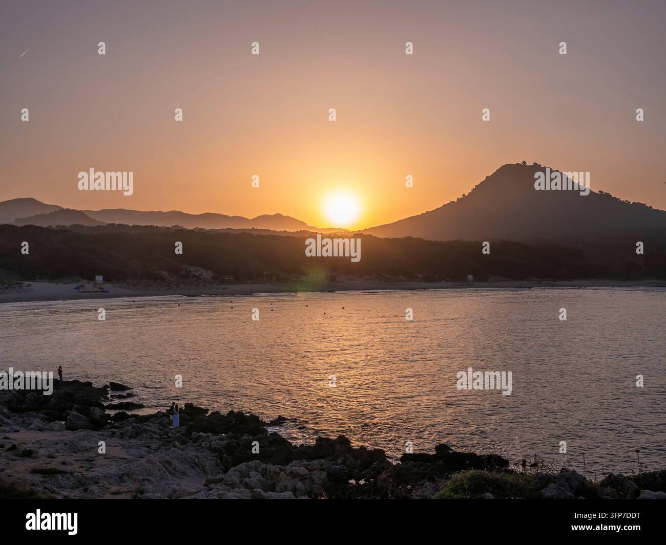 Un tranquillo tramonto su Cala Rajada, Maiorca, mare calmo con una silhouette di colline e una costa rocciosa, Maiorca Foto Stock