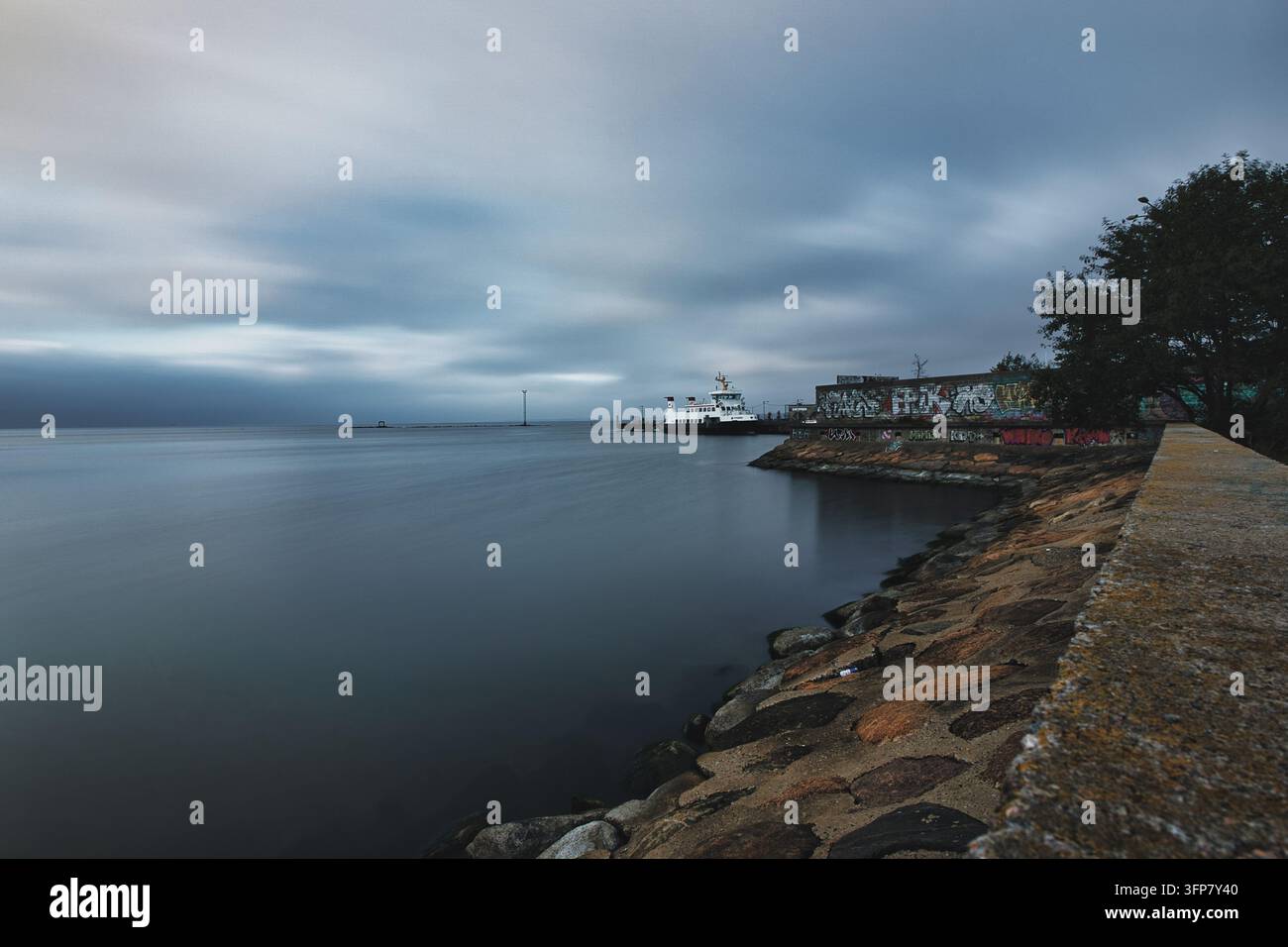 Vista costiera a lunga esposizione di mare liscio e riva rocciosa sotto un cielo nuvoloso Foto Stock