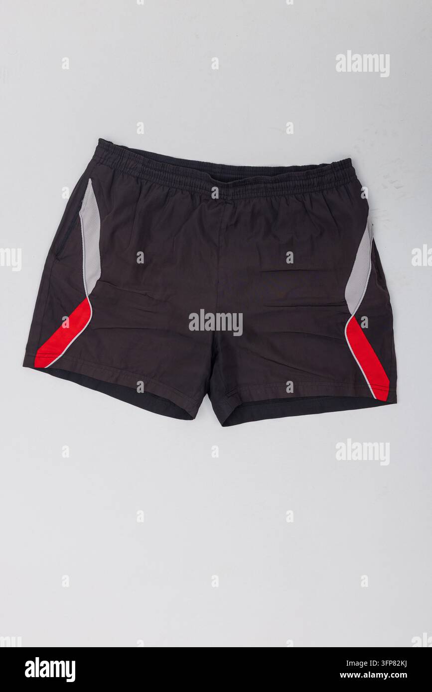 Pantaloncini sportivi neri da uomo con accenti laterali rossi e grigi posati a terra su sfondo studio bianco. Scatto prodotto ideale per abbigliamento sportivo, palestra Foto Stock