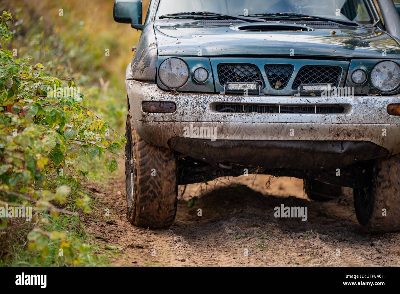 Ante di un 4x4 coperto di fango con fari rotondi, lampade ausiliarie e pneumatici robusti su un sentiero boschivo dissestato, mostra l'attrezzatura del veicolo per il fuoristrada ricreativo Foto Stock