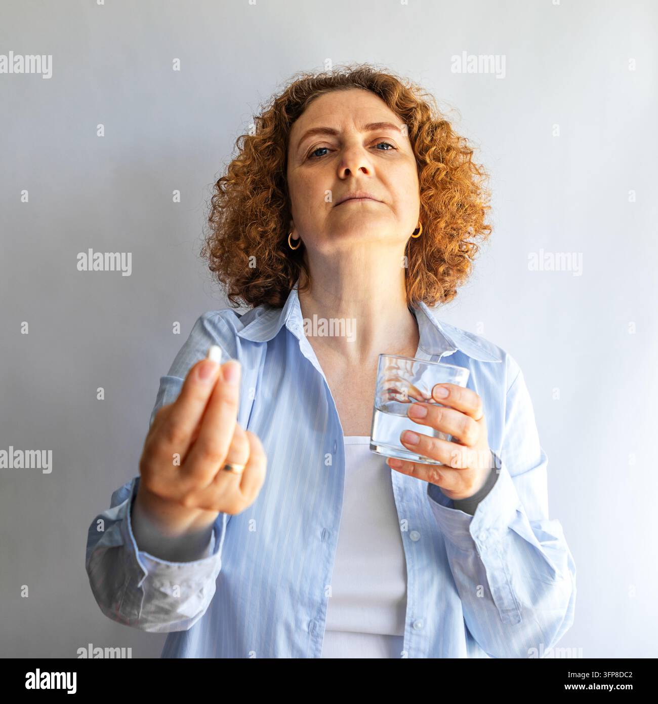 Donna di mezza età che prende una pillola con un bicchiere d'acqua mostrando la routine di assistenza sanitaria e cura di sé a casa Foto Stock
