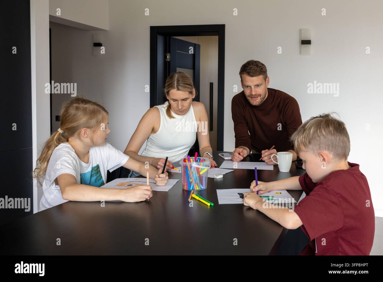 Famiglia felice con due bambini che giocano insieme a un gioco di disegno a casa. Tempo di qualità Foto Stock
