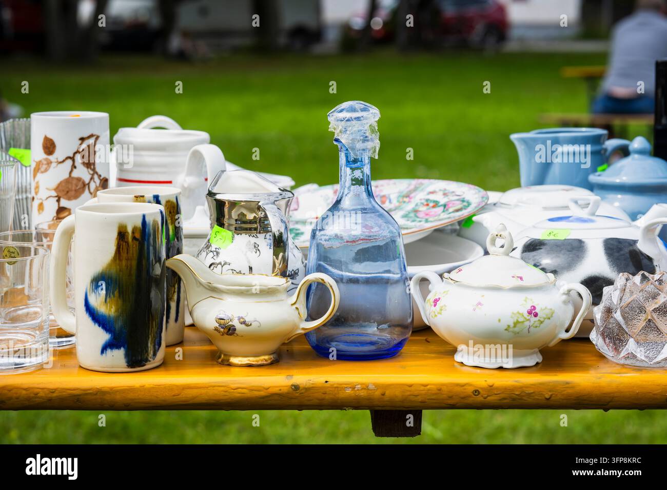 Stoviglie vintage esposte in un mercatino delle pulci all'aperto, con teiere di porcellana, tazze di ceramica, vetreria, una bottiglia di vetro blu, piatti floreali. Foto Stock