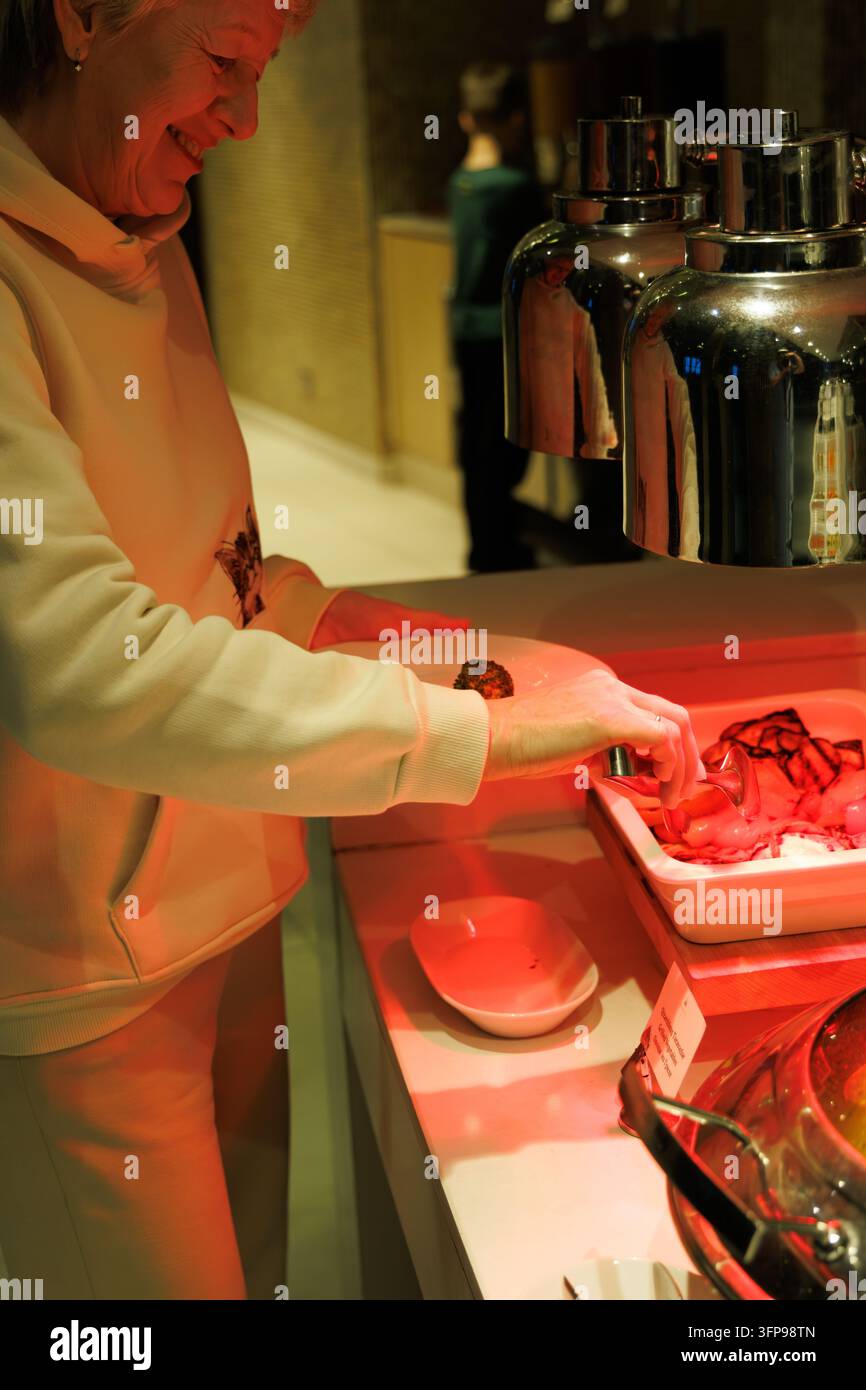 Ritratto verticale di una donna matura sorridente che usa delle pinze sotto una lampada termica durante un buffet cena in un ristorante di lusso di un resort. Foto Stock