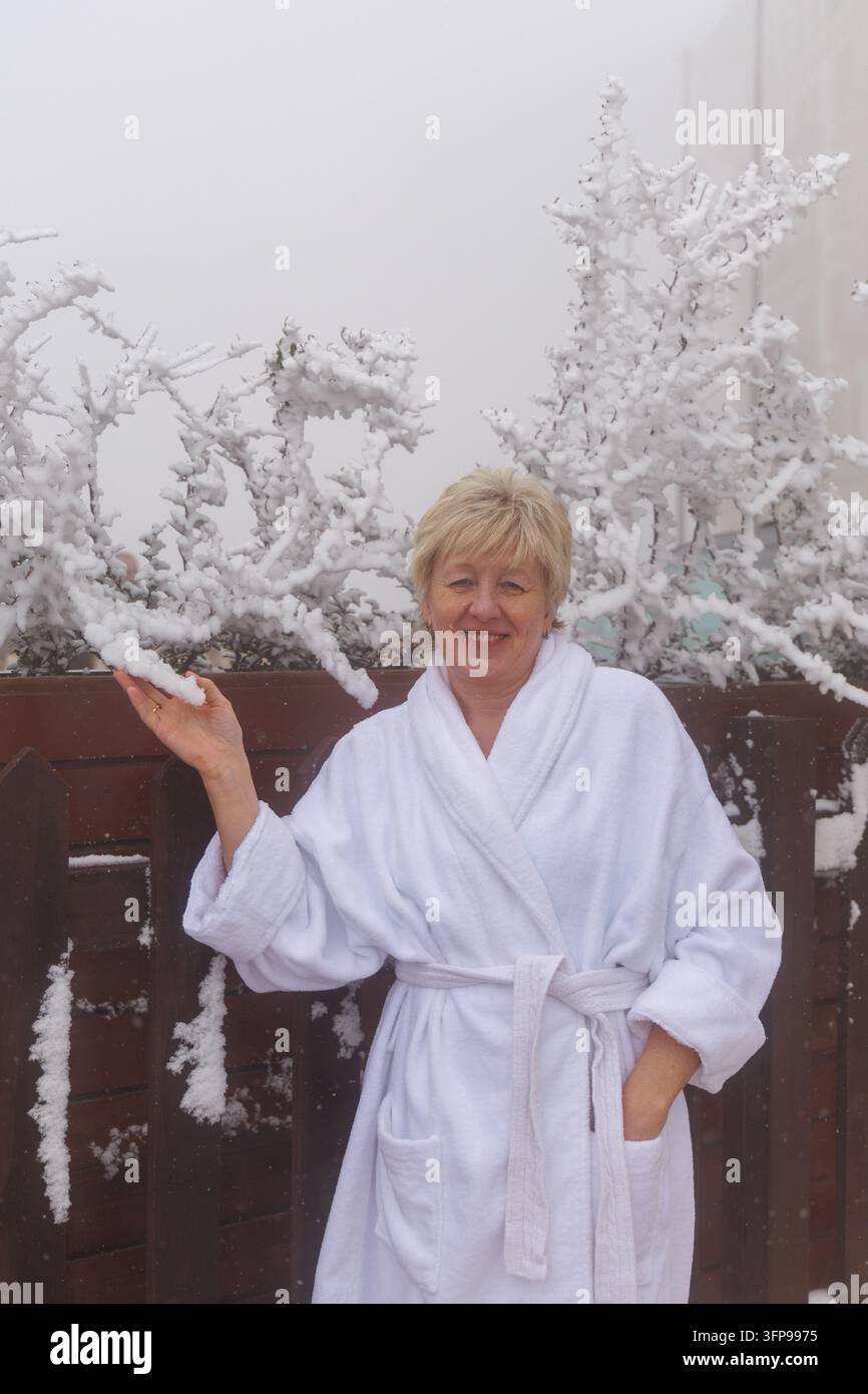 Ritratto verticale di una donna anziana sorridente in accappatoio che si gode le vacanze invernali in un resort di benessere di lusso. Foto Stock