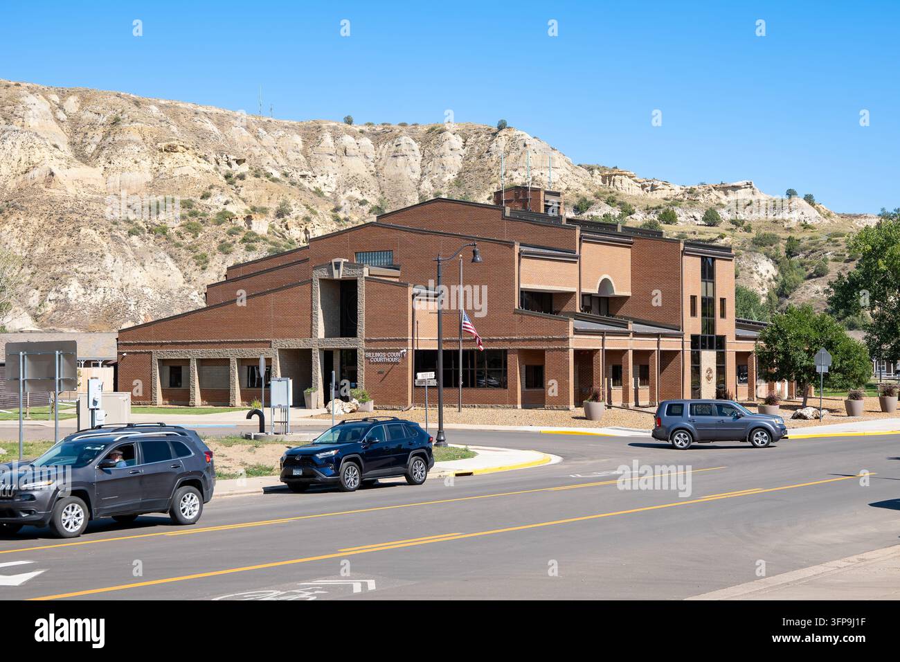 MEDORA, ND - 26 AGOSTO 2026: Edificio in mattoni del tribunale della contea di Billings con le colline delle Badlands sullo sfondo e auto in strada, Medora, North Dakota. Foto Stock