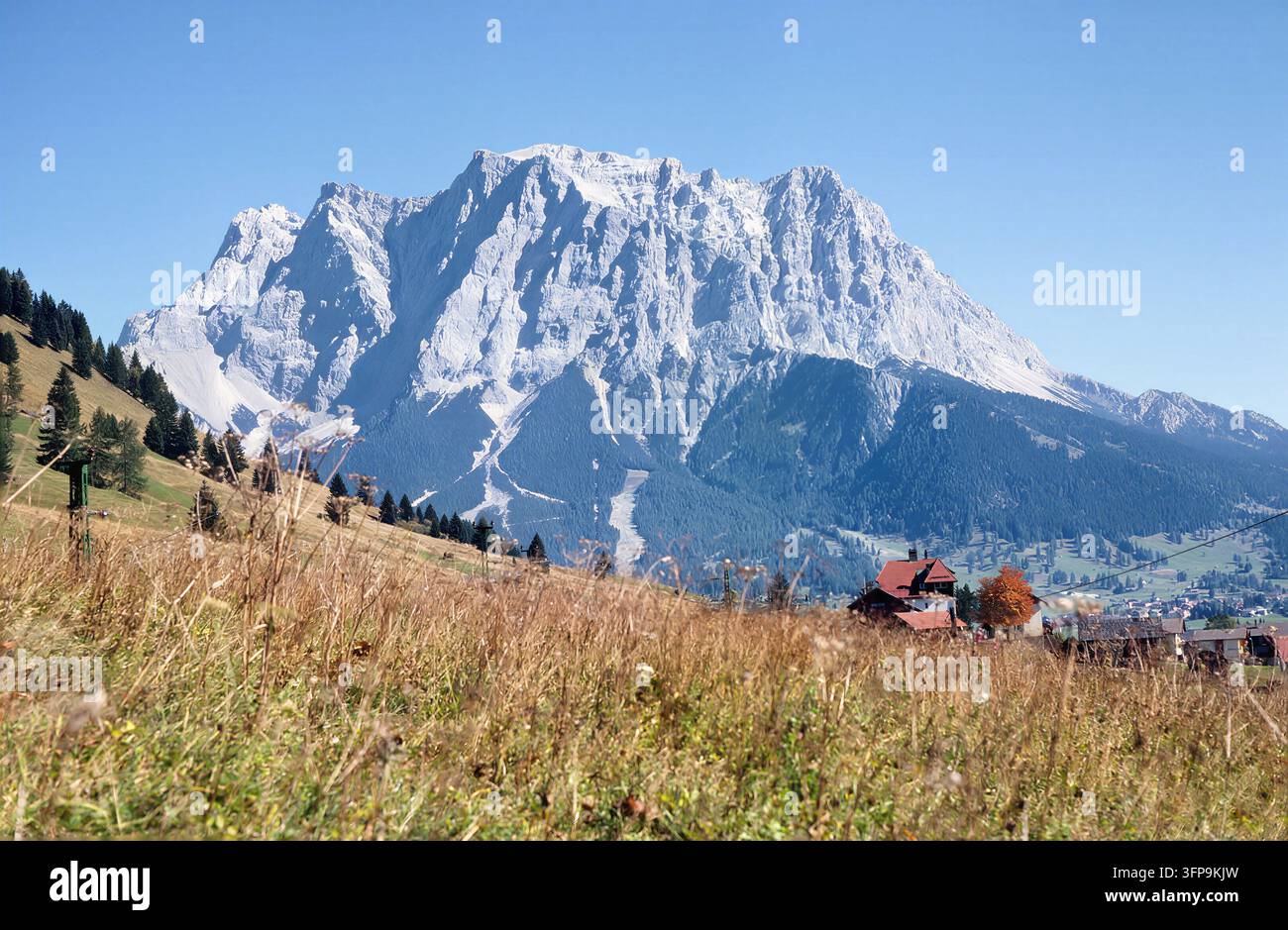 Una vista panoramica mette in mostra l'imponente montagna Sonnenspitze, il cui picco innevato domina lo skyline. Prati rigogliosi punteggiati da edifici tradizionali Foto Stock