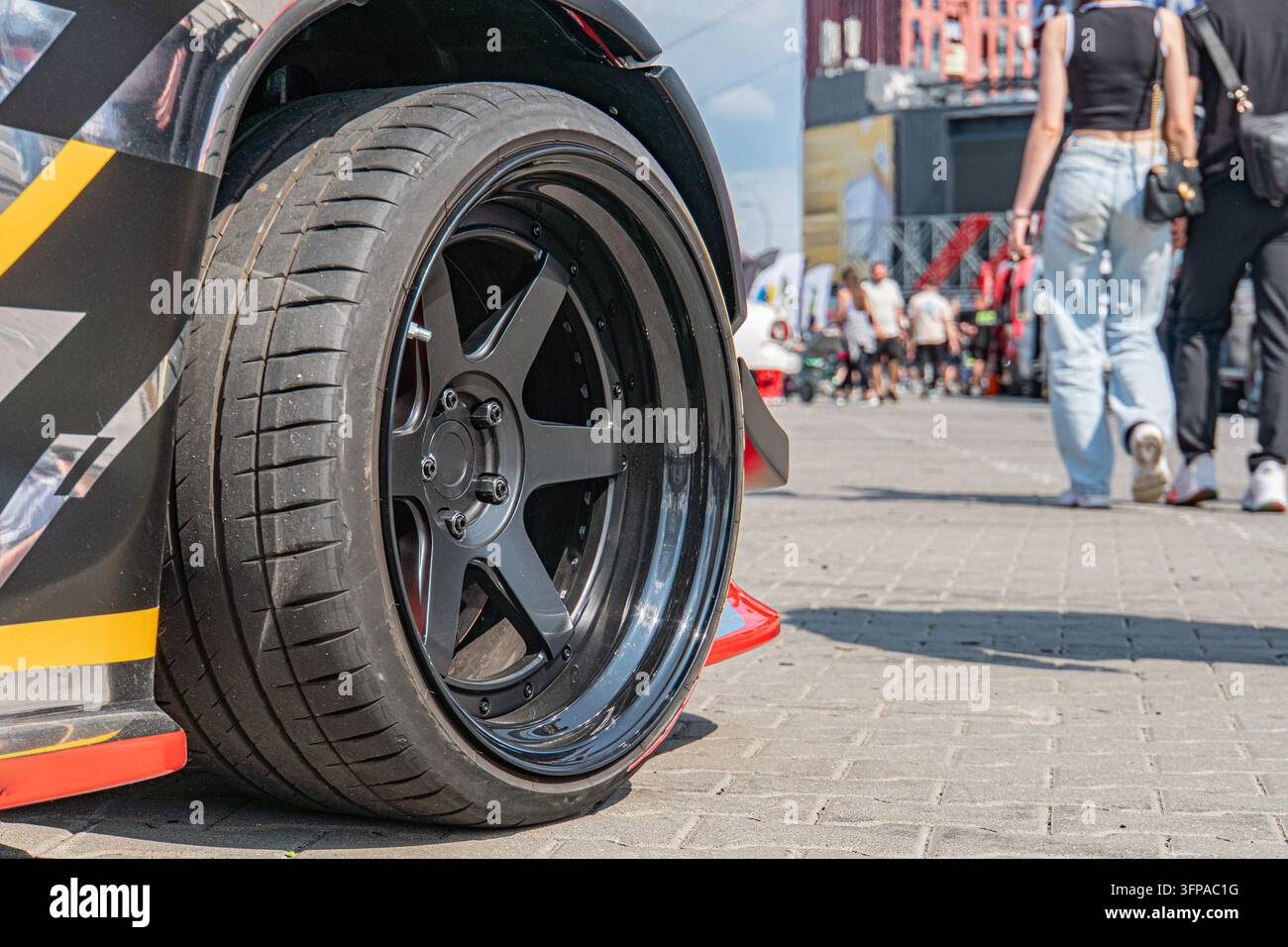Prima vista di un pneumatico per auto nero e rosso con cerchione lucido, più motivi, testo ileggibile sul fianco Pneumatico parzialmente visibile sullo sfondo di una carrozzeria decorata Foto Stock