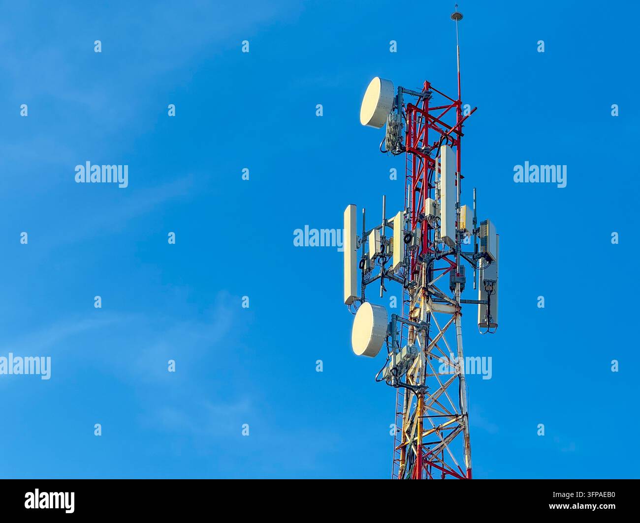 Alto traliccio di telecomunicazioni rosso e bianco con più antenne contro il cielo blu – Infrastruttura di rete mobile Foto Stock