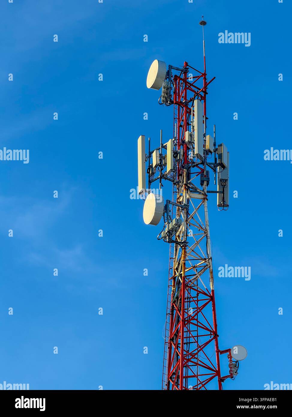 Alto traliccio di telecomunicazioni rosso e bianco con più antenne contro il cielo blu – Infrastruttura di rete mobile Foto Stock