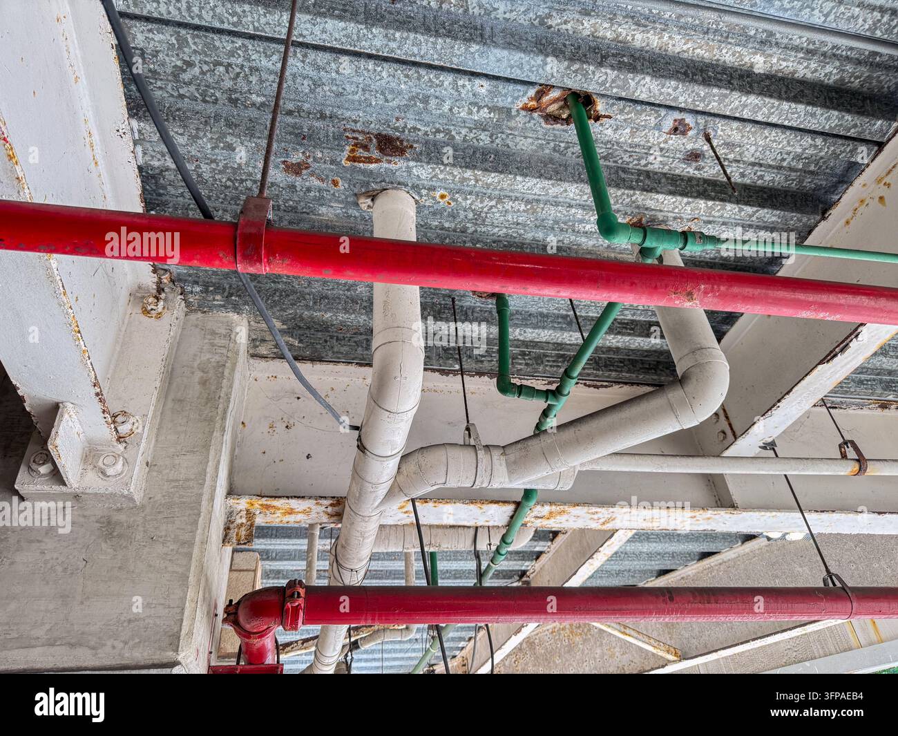 Tubi industriali colorati rosso verde bianco sotto soffitto in lamiera ondulata – Dettaglio dell’infrastruttura idraulica urbana Foto Stock