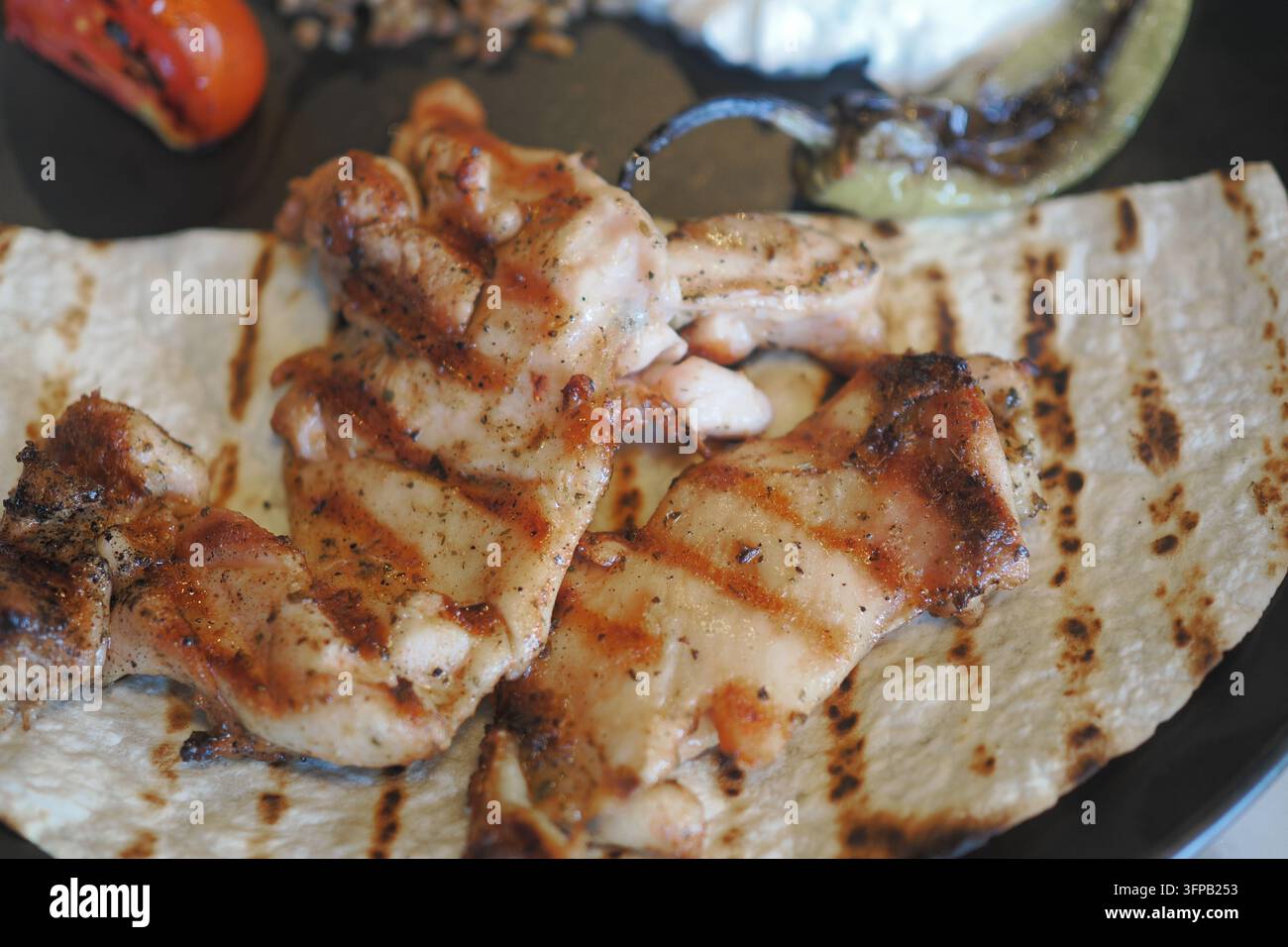 Pezzetti di pollo grigliato su una tortilla con verdure su un piatto Foto Stock
