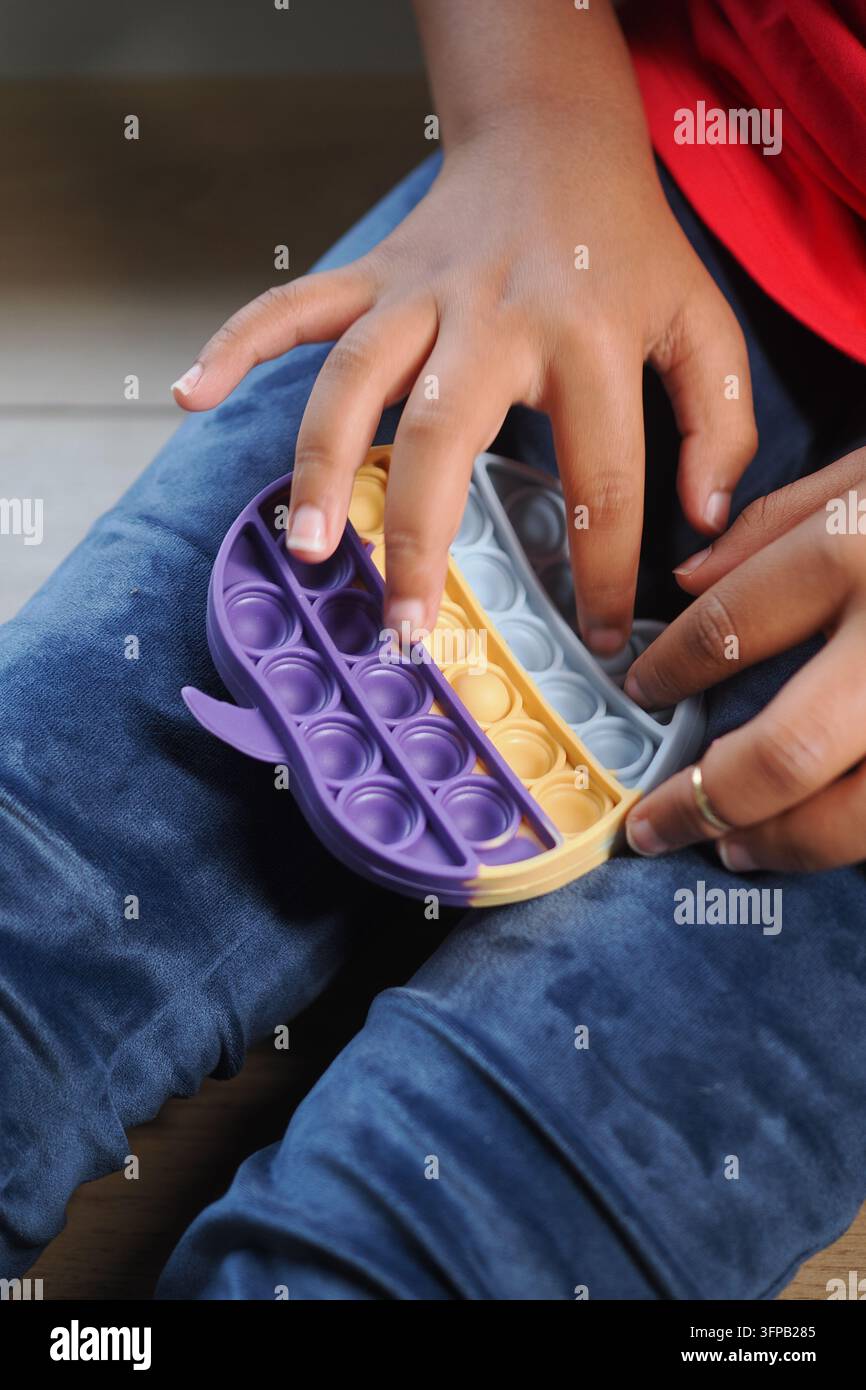 Un bambino gioca con un giocattolo pop it mentre è seduto sul pavimento in casa Foto Stock