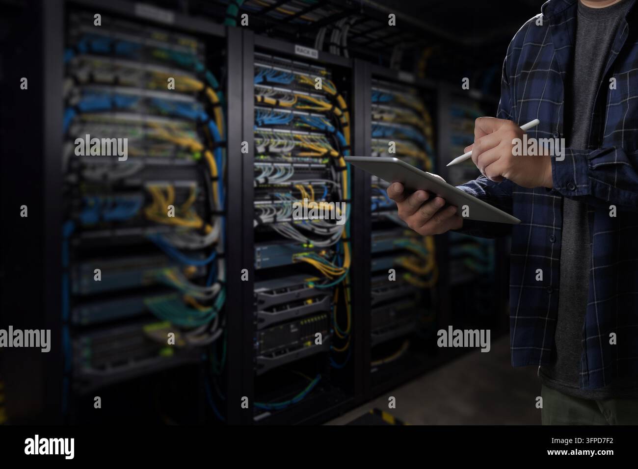 Ingeniero uomo supporto IT utilizzando tablet e stilo accanto ai rack dei server in un data center, supportando il monitoraggio della rete, la revisione dell'infrastruttura IT e la tecnologia Foto Stock