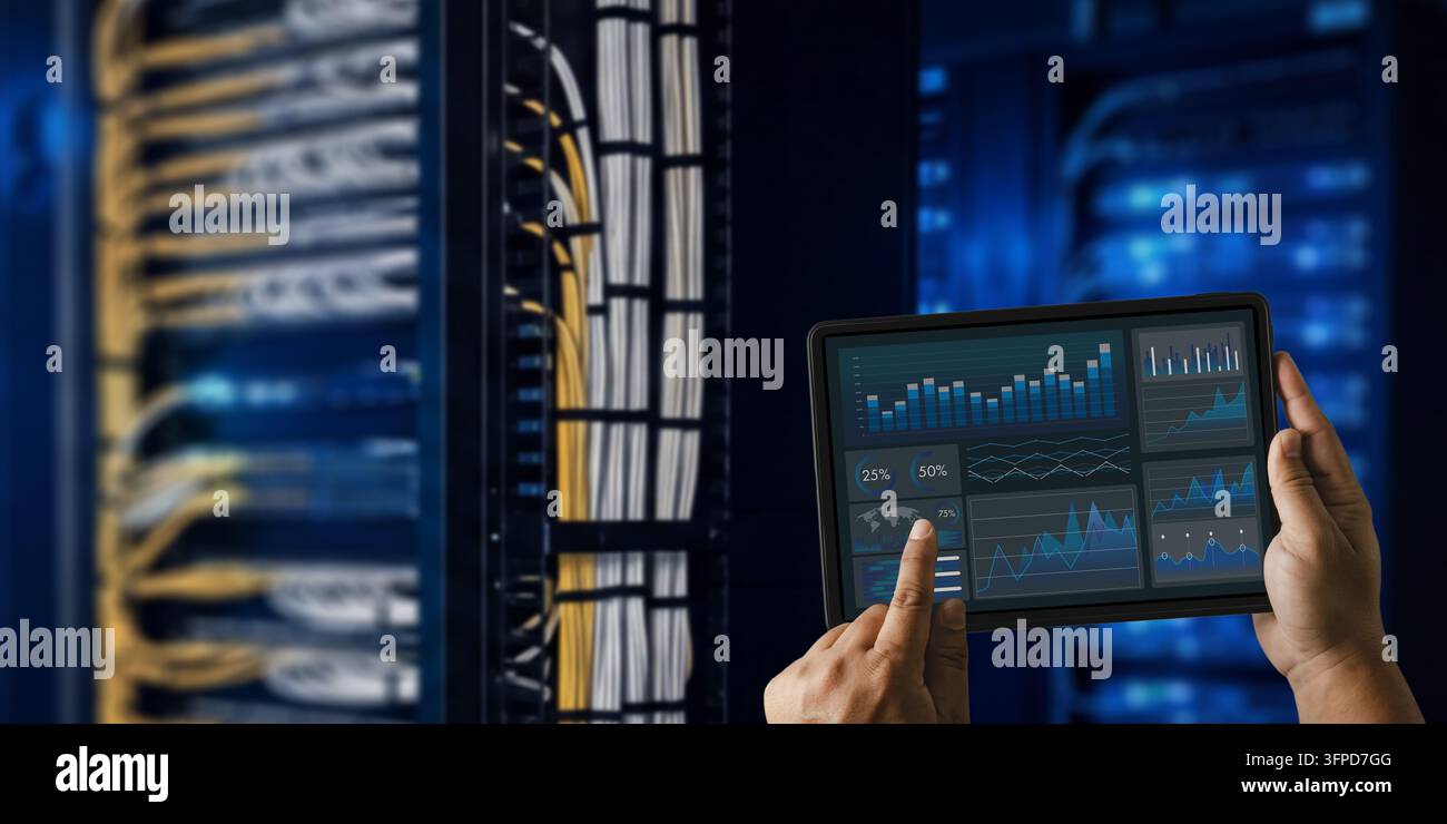 Ingeniero uomo supporto IT che tiene un tablet con dashboard analitico accanto ai rack dei server, monitorando le prestazioni della rete e rivedendo i sistemi del data center Foto Stock
