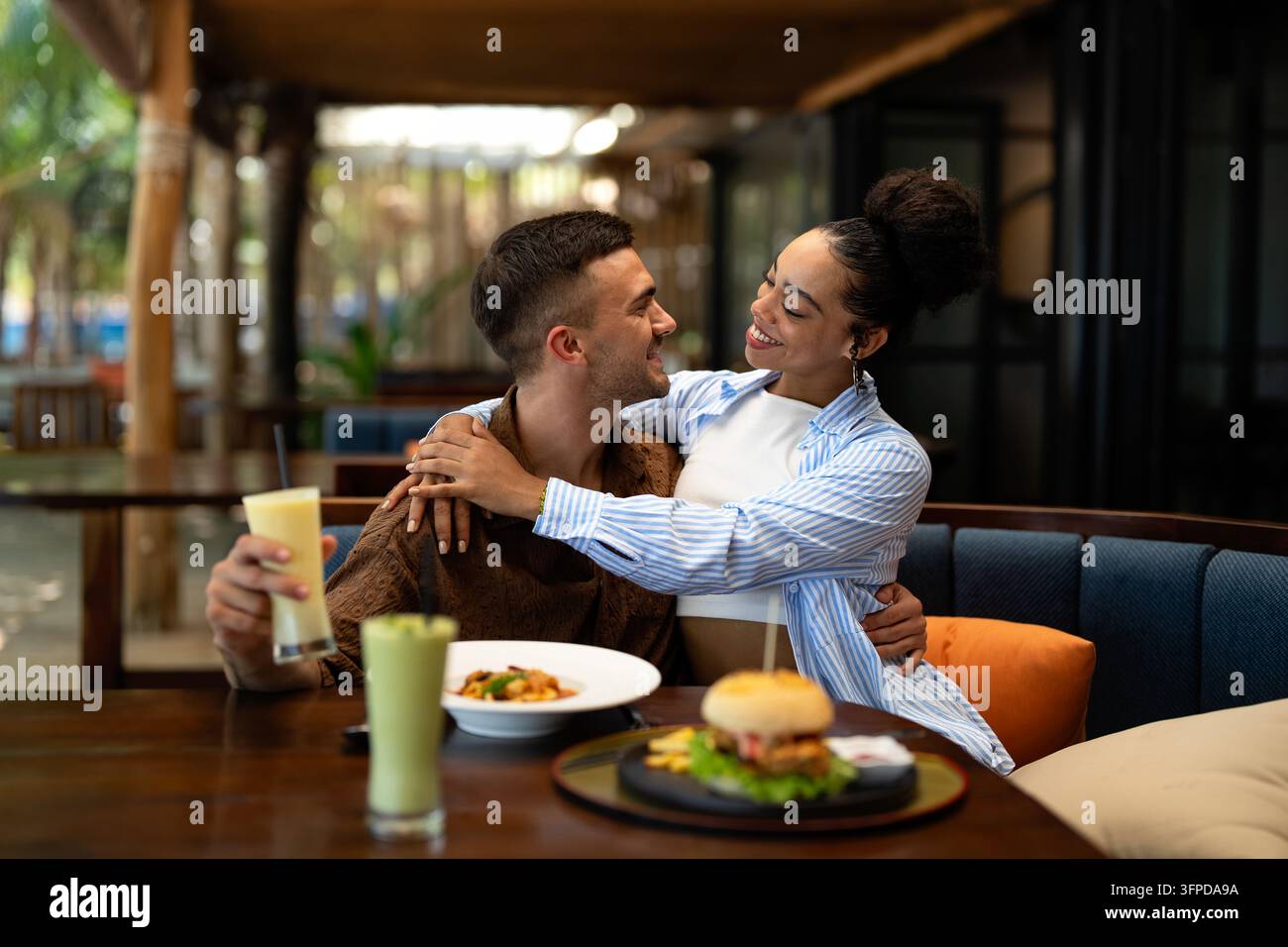 Coppie diverse in un appuntamento gastronomico si godono una cena informale e un momento al telefono, condividendo le vibrazioni soleggiate e le bevande Foto Stock