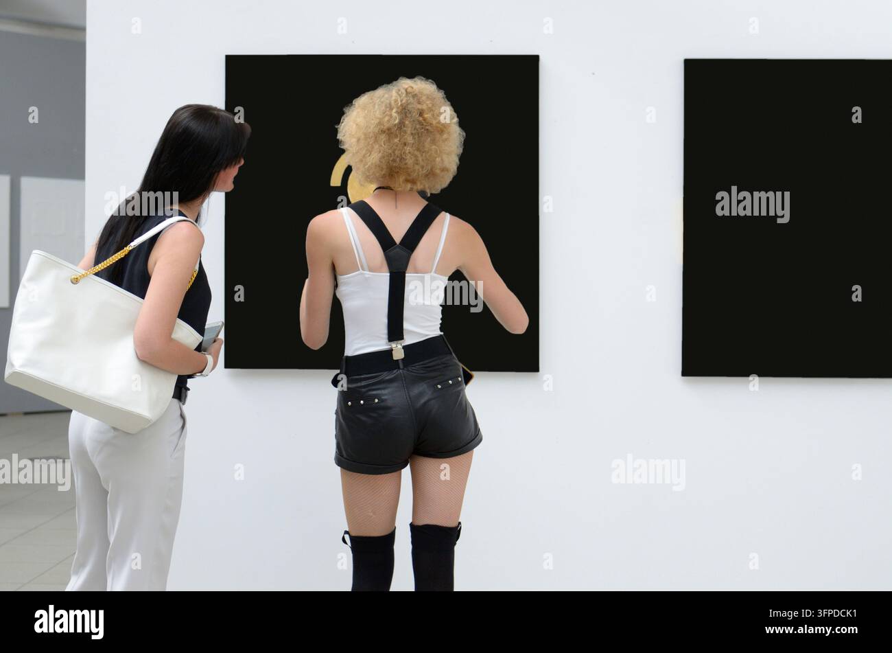 Due giovani donne che osservano grandi tele nere in una galleria d'arte, aggrappandosi a qualsiasi cosa nel nulla nero. Foto Stock