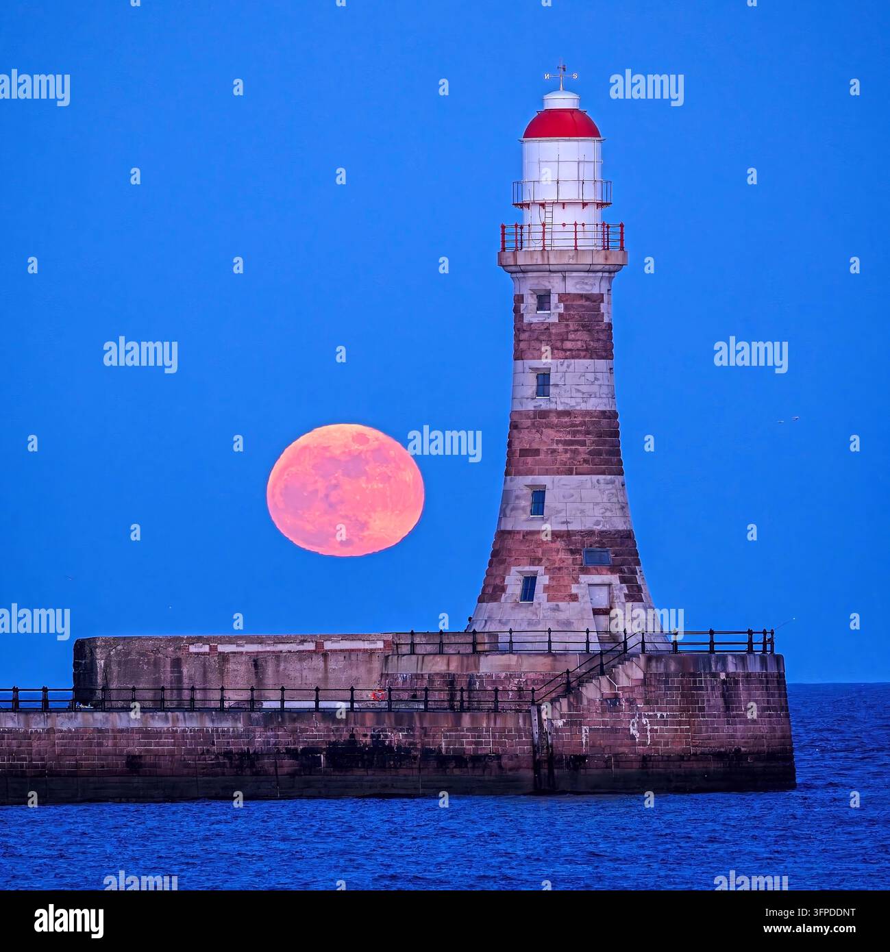 Una vista della luna piena (luna dell'annata) che sorge in un cielo sereno al crepuscolo sopra il Roker Pier & Faro a Sunderland, Tyne & Wear Foto Stock