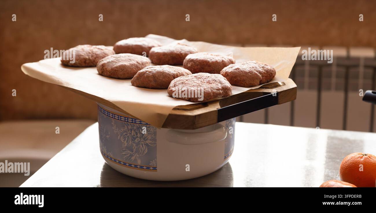 Cotolettes crude fatte in casa su un tagliere di legno in una calda cucina casalinga Foto Stock