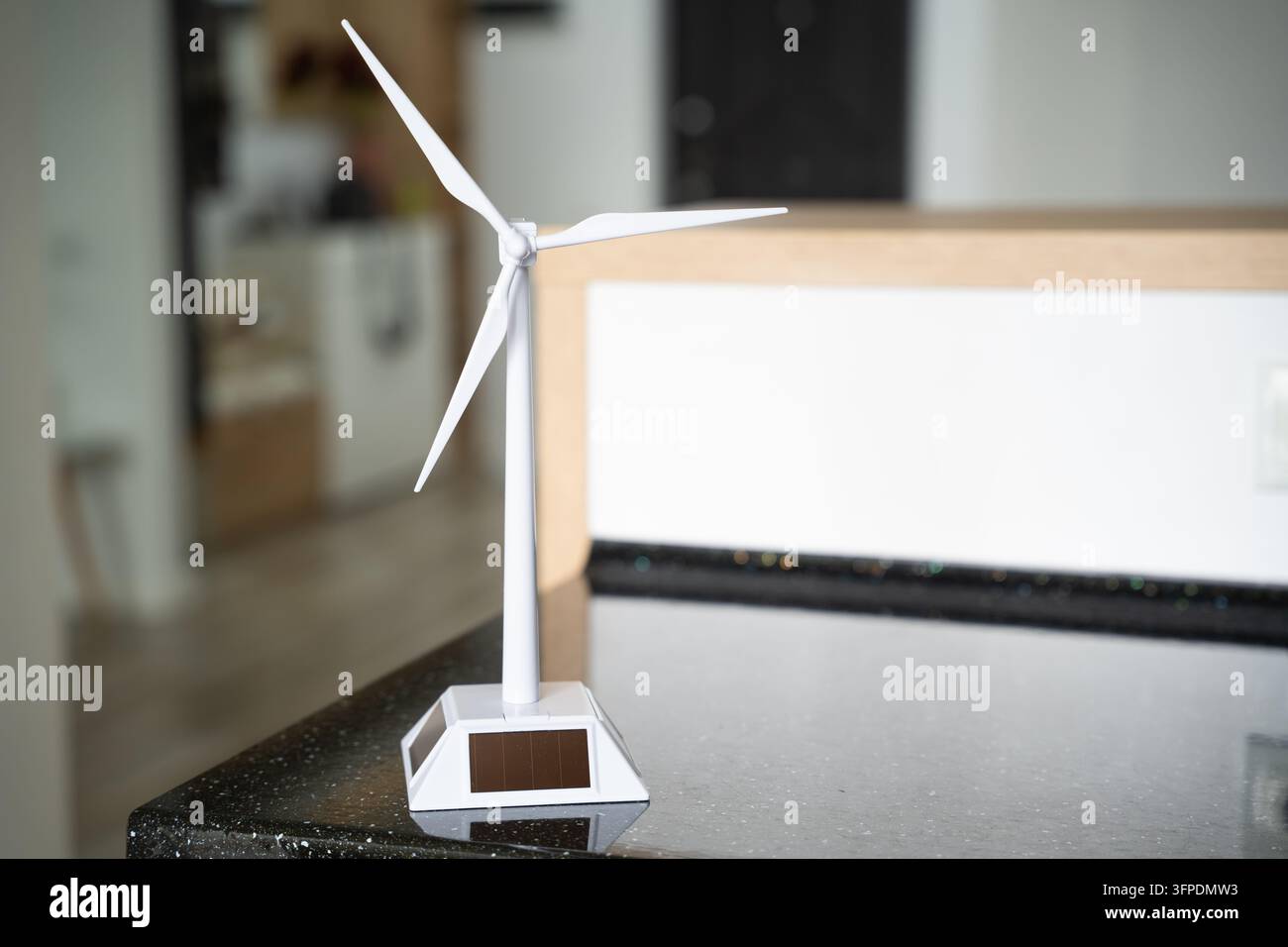 Piccolo modello di turbina eolica in piedi su un tavolo scuro in un ambiente interno moderno. Educazione sull'energia pulita, energia rinnovabile e transizione energetica. Foto Stock