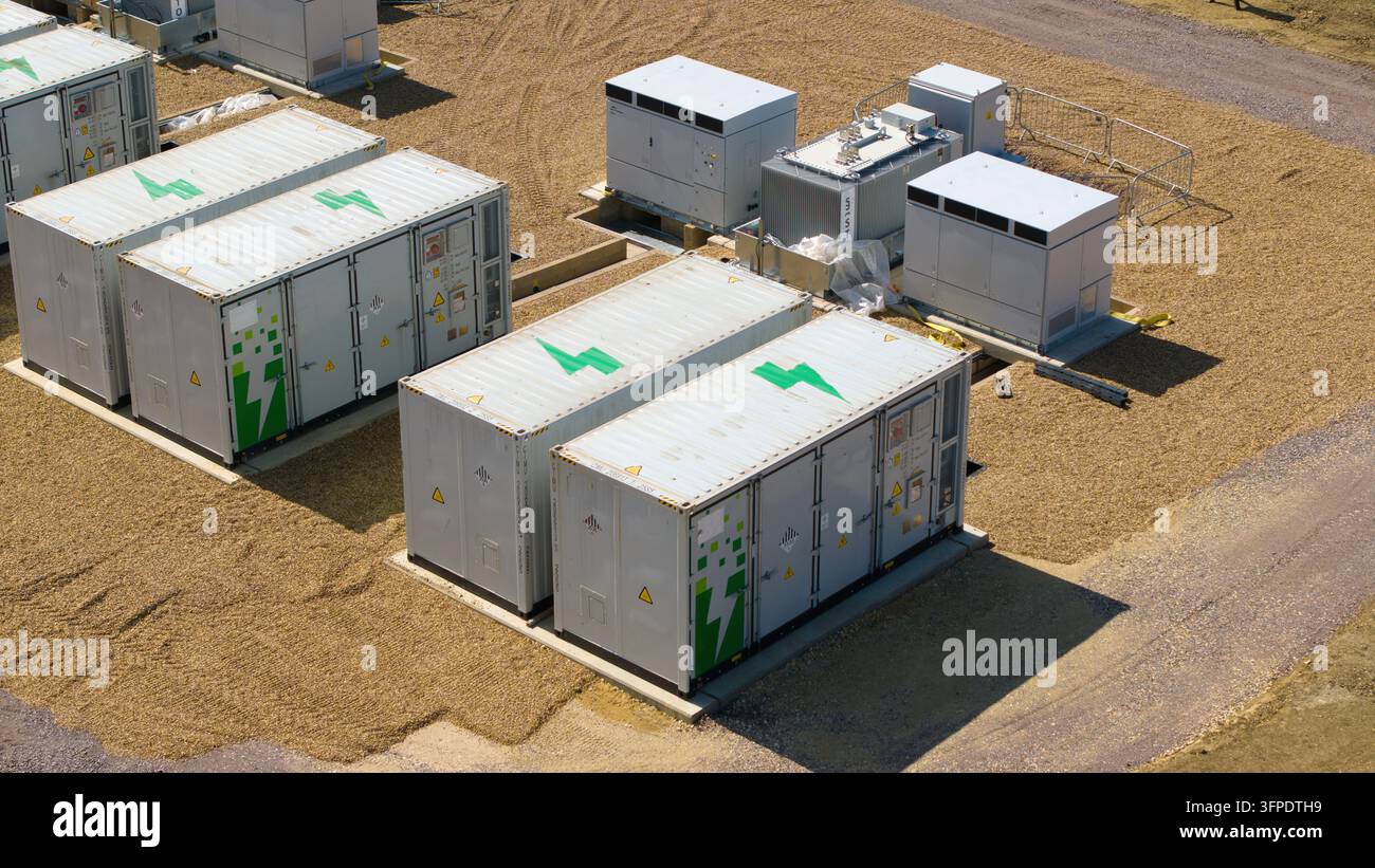 Vista aerea di sistemi di accumulo di energia a batteria con contenitori industriali bianchi e loghi a forma di fulmine verde su un sito di ghiaia a Eaton Socon, E Foto Stock