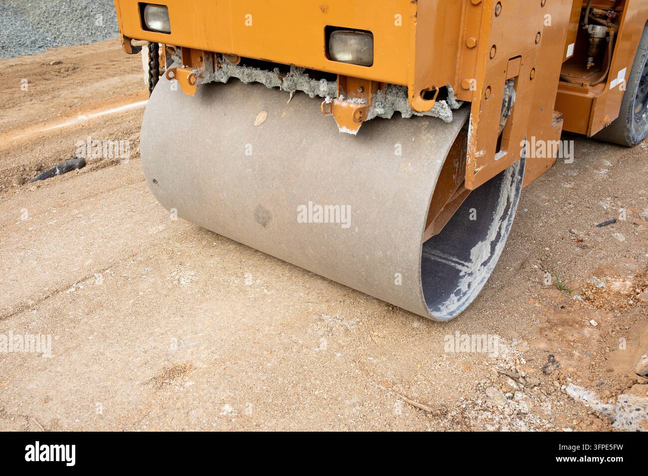 Rullo vibrante appiattisce un sentiero di terra durante i lavori infrastrutturali comunali diurna. La macchina compattatrice gialla elabora la terra sciolta mentre mantiene Foto Stock