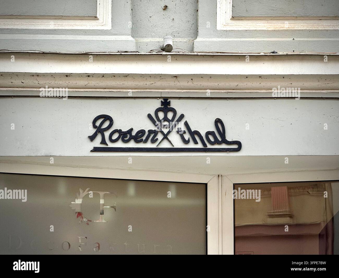 Fotografia in primo piano del logo nero Rosenthal montato sopra l'ingresso di un negozio, con tipografia in stile script e un'icona a forma di corona - Immagine stock catturata con smartphone