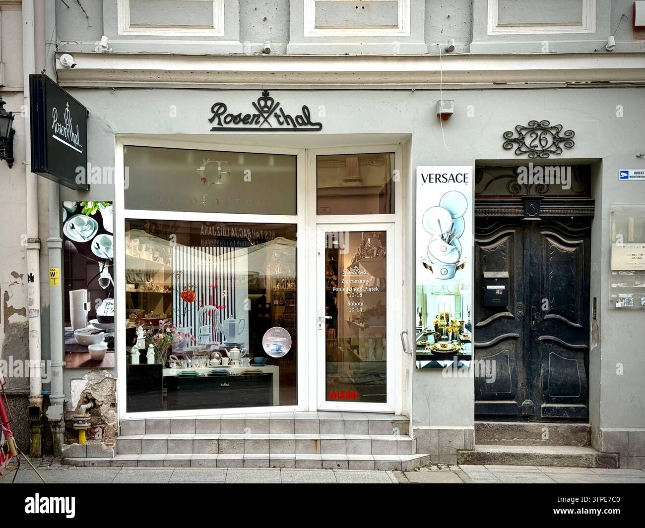 Fotografia frontale della facciata di un negozio Rosenthal con grandi vetrine, cornici bianche, loghi del marchio neri e un pannello pubblicitario Versace - Immagine stock catturata con smartphone