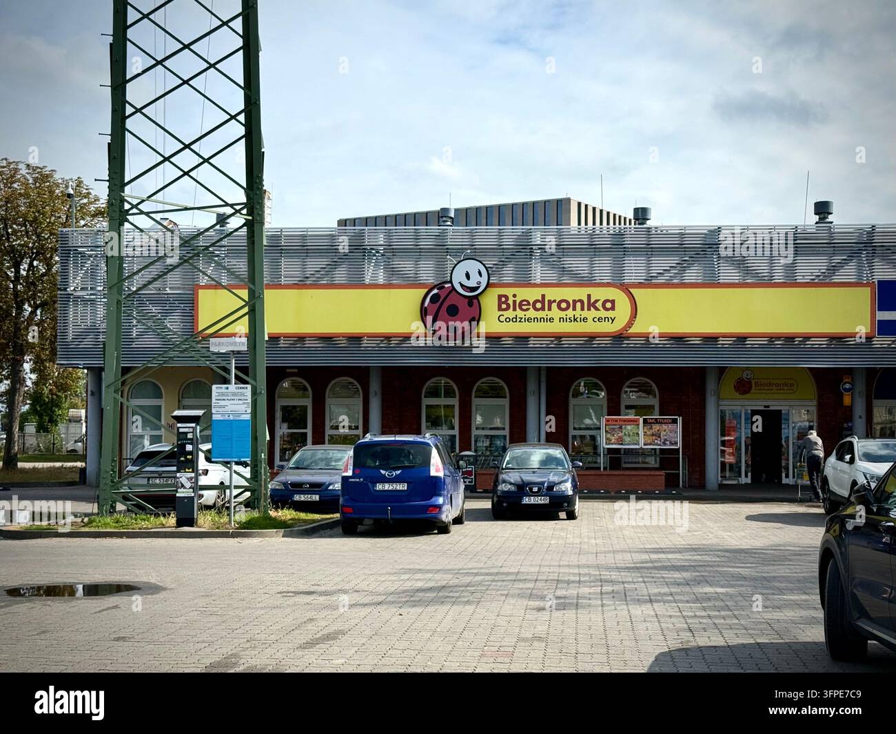 Vista esterna di un edificio del supermercato Biedronka a Bydgoszcz con il suo prominente cartello logo giallo, auto parcheggiate - Immagine stock catturata con smartphone