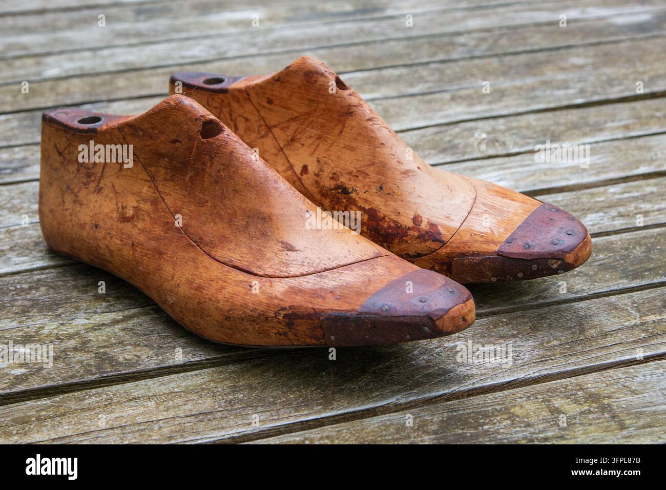 Modelli tradizionali di scarpe in legno usati nella calzatureria, che mostrano superfici consumate e artigianalità, fotografati su assi di legno stagionate. Foto Stock