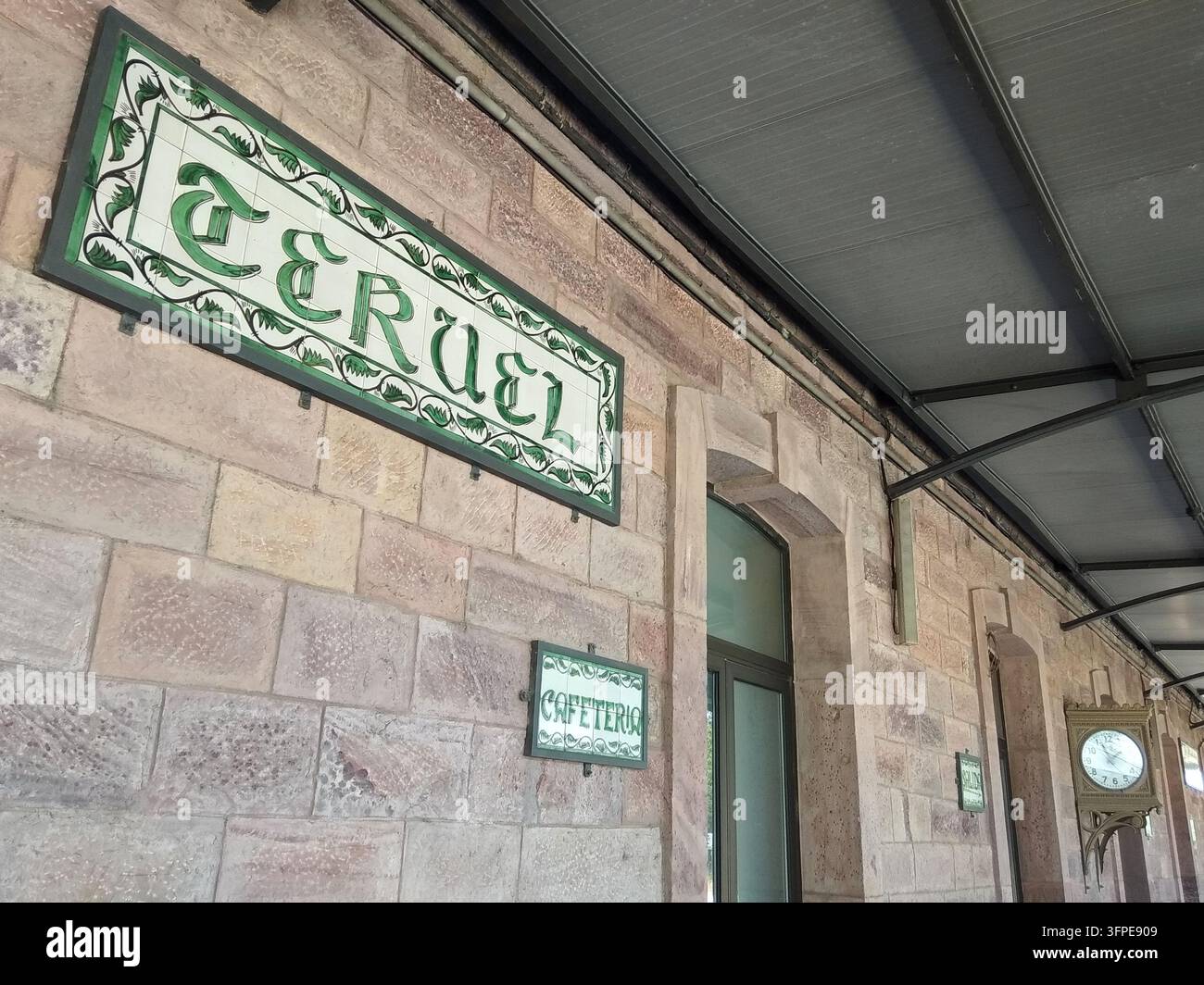 Facciata in calcare della storica stazione ferroviaria di Teruel, Spagna, con i suoi emblematici cartelli in ceramica neo-mudéjar bianchi e verdi e l'orologio tipico della stazione. Foto Stock