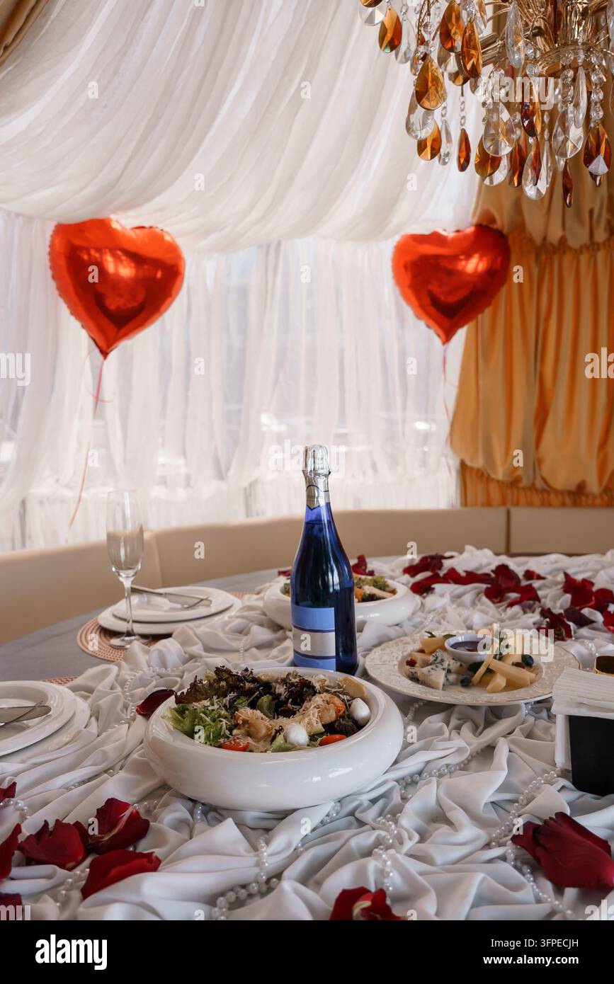 Configurazione elegante del banchetto con petali di rosa e stoviglie raffinate per la fotografia di celebrazioni intime Foto Stock