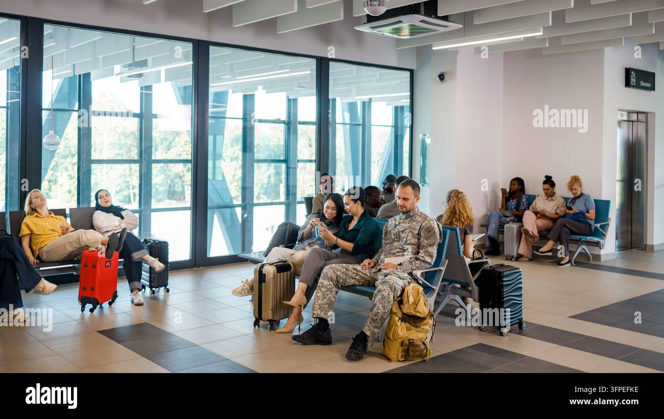 Diverse persone attendono in un terminal aeroportuale accanto ai loro bagagli. Alcuni sono al telefono mentre altri chiacchierano. Foto Stock