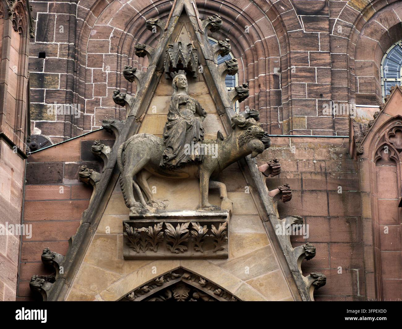 Scultura in pietra di una donna incoronata in sella a un leone inserita in un frontone triangolare gotico sulla facciata della cattedrale di Worms, Germania. Foto Stock