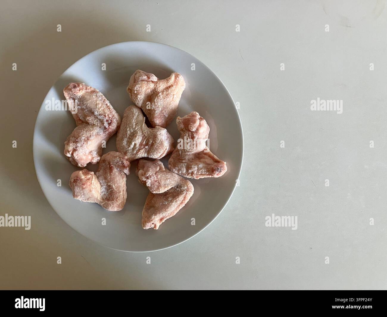 Alette di pollo crude su piatto bianco con spazio libero Foto Stock