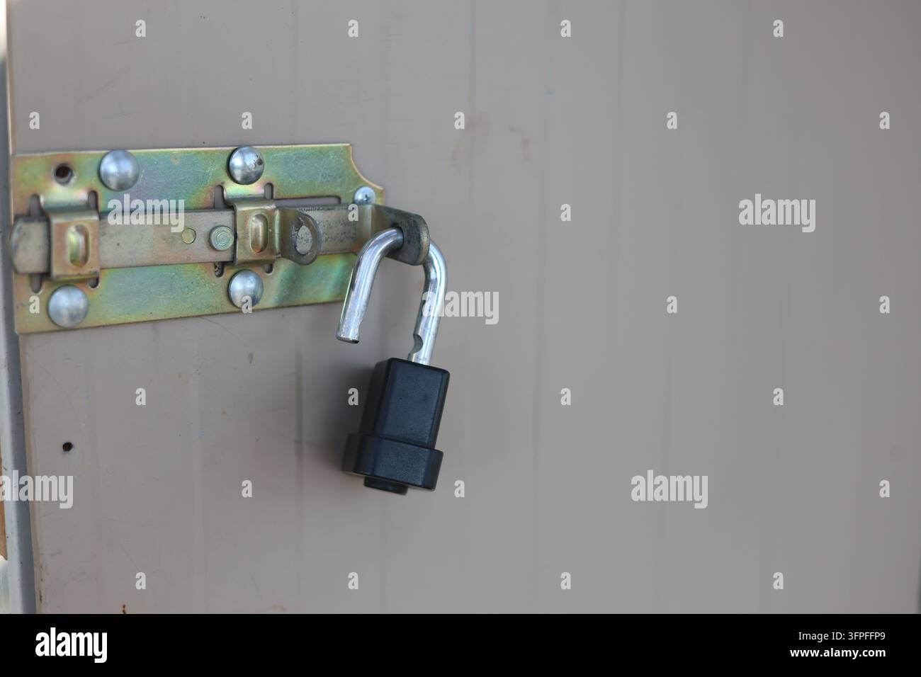 Prima di un lucchetto nero fissato su una serratura a slitta in metallo sulla porta di un capanno beige Foto Stock