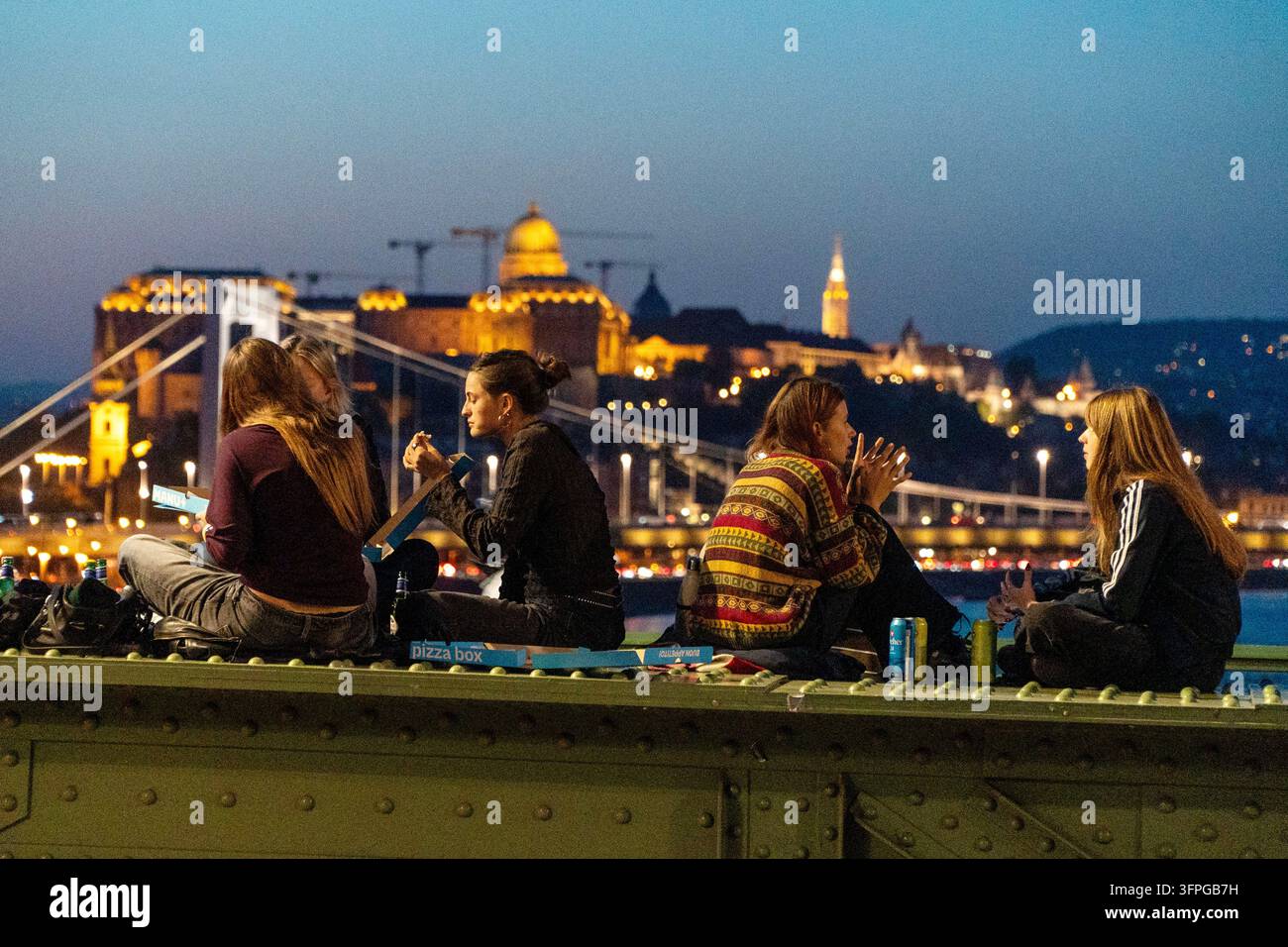 Le persone siedono sul Ponte delle Catene al crepuscolo con il quartiere del castello dietro di loro a Budapest, Ungheria, Foto Stock