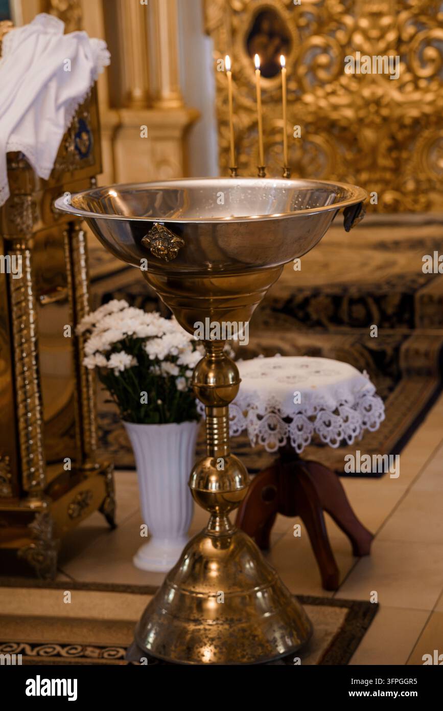 Bacino di acqua santa in un santuario religioso storico con candele e fiori bianchi per i servizi di culto Foto Stock