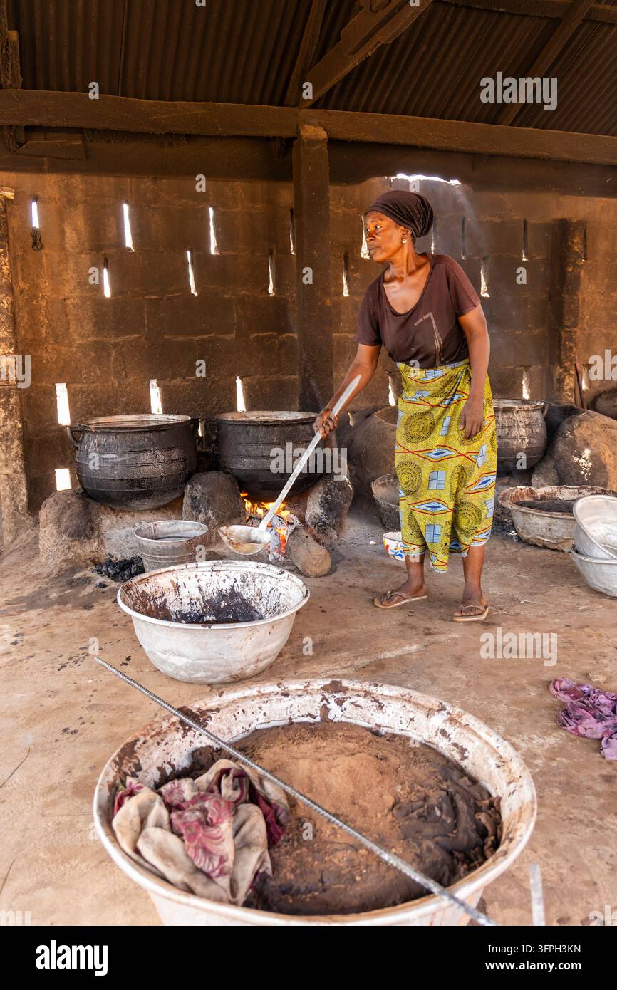 Donna che mescola burro di karité in grandi pentole su un fuoco aperto in una bottega tradizionale, Regione Settentrionale, Tamale, Ghana Foto Stock