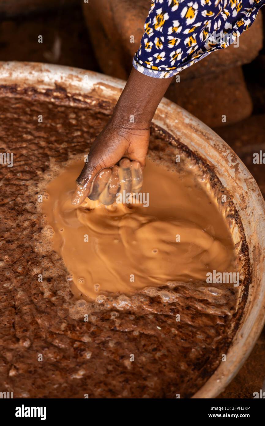 Primo piano di una mano che impasta una pasta di burro di karité in un grande bacino di metallo, Regione Settentrionale, Tamale, Ghana Foto Stock