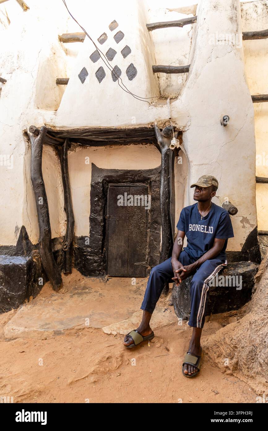 Uomo seduto all'ingresso in legno di una moschea tradizionale in fango decorata con motivi a diamante, regione di Savannah, Larabanga, Ghana Foto Stock