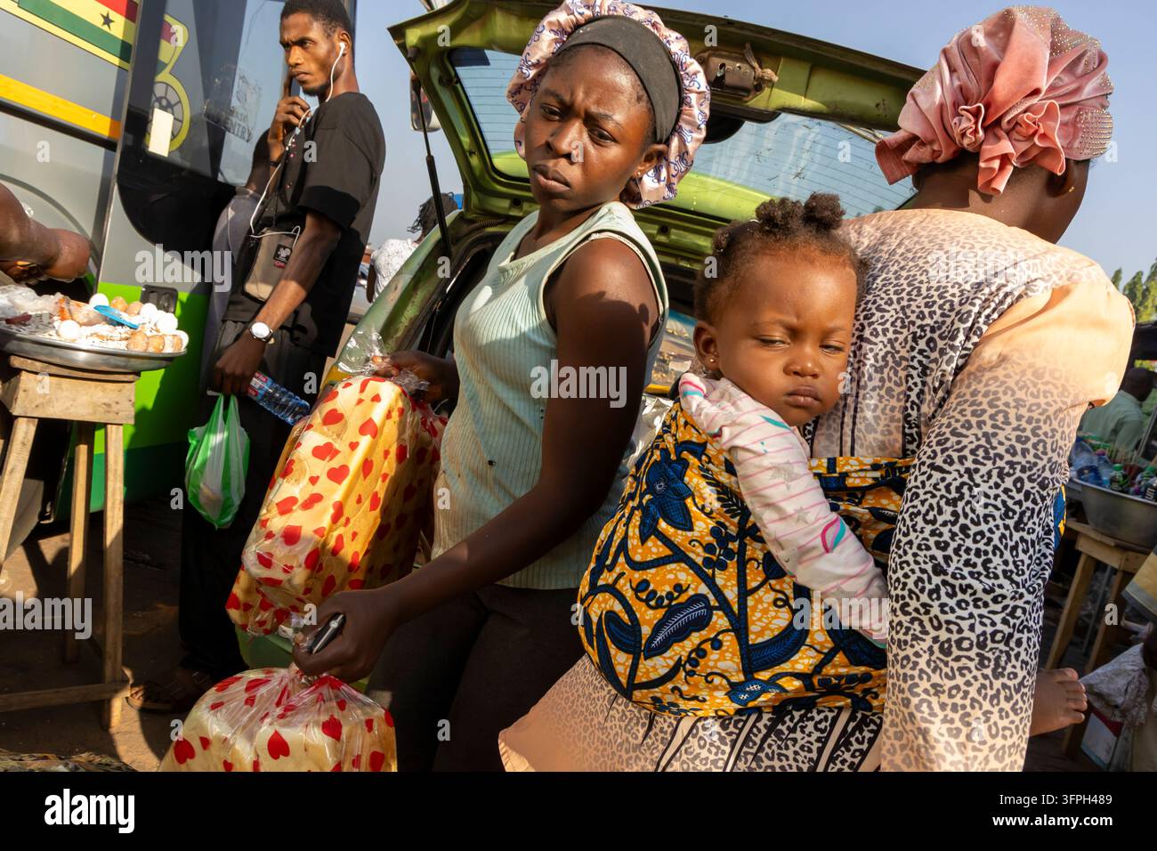 Donne che portano un bambino e pane in un affollato mercato di strada, regione di Bono East, Kintampo, Ghana Foto Stock