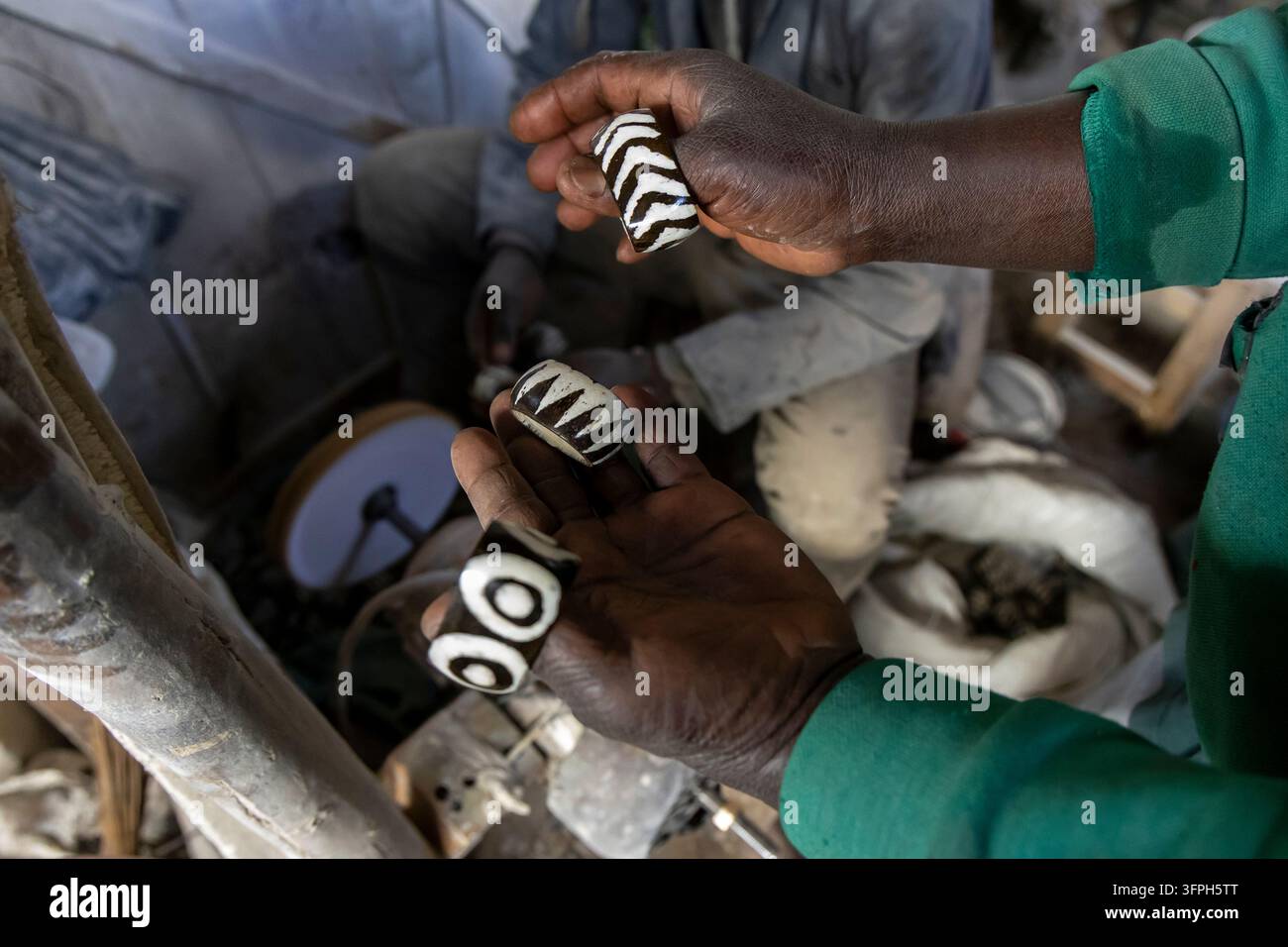 Mani che tengono tre anelli d'osso intagliati con motivi a zigzag e cerchi bianchi e neri in una bottega della zona di Kibera che produce souvenir per turisti con l'osso Foto Stock