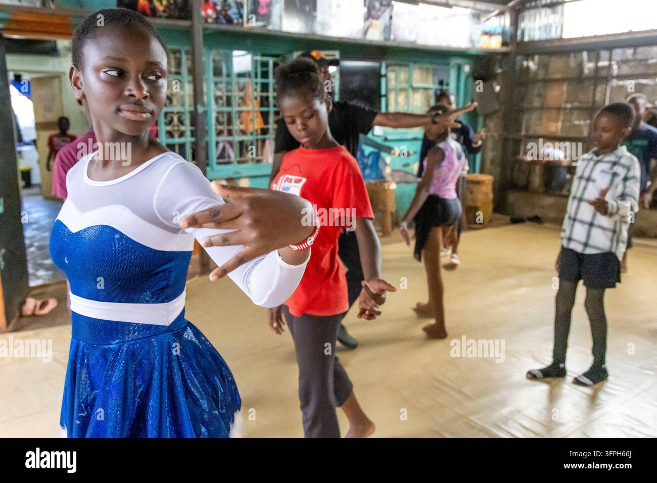 Ragazza in un costume blu scintillante con il braccio teso e bambini che danzano alla scuola di balletto di Kibera, Contea di Nairobi, Nairobi, Kenya Foto Stock