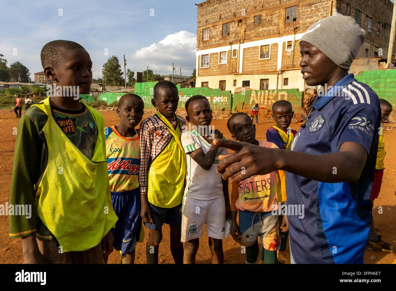 Allenatrice di calcio donna in una maglia del Manchester United che istruisce un gruppo di ragazzi su un campo di terra a Kibera, Contea di Nairobi, Nairobi, Kenya Foto Stock