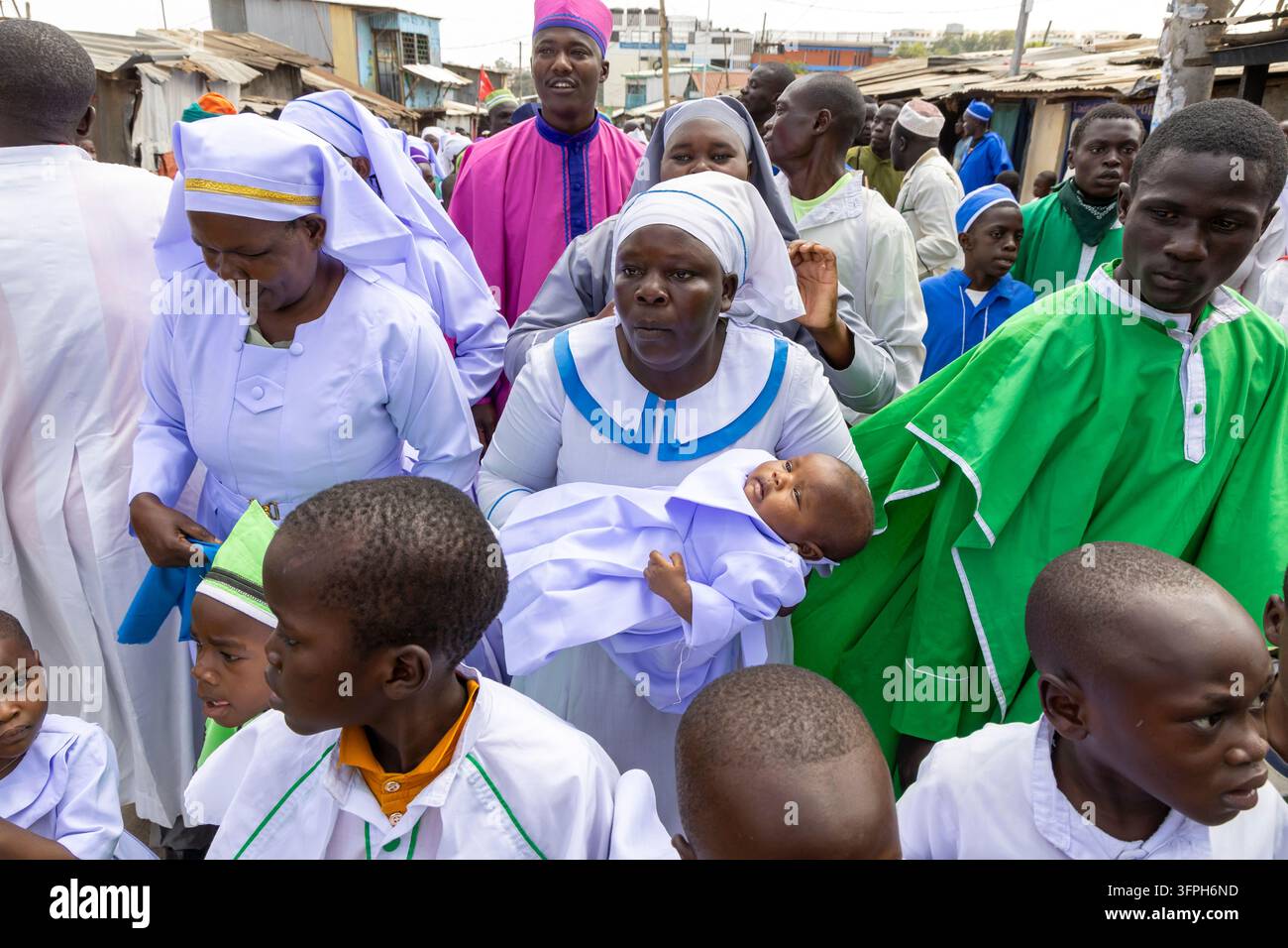 Donna in abito bianco che tiene un bambino in una veste lilla durante una processione battesimale in una strada di Kibera, Contea di Nairobi, Nairobi, Kenya Foto Stock
