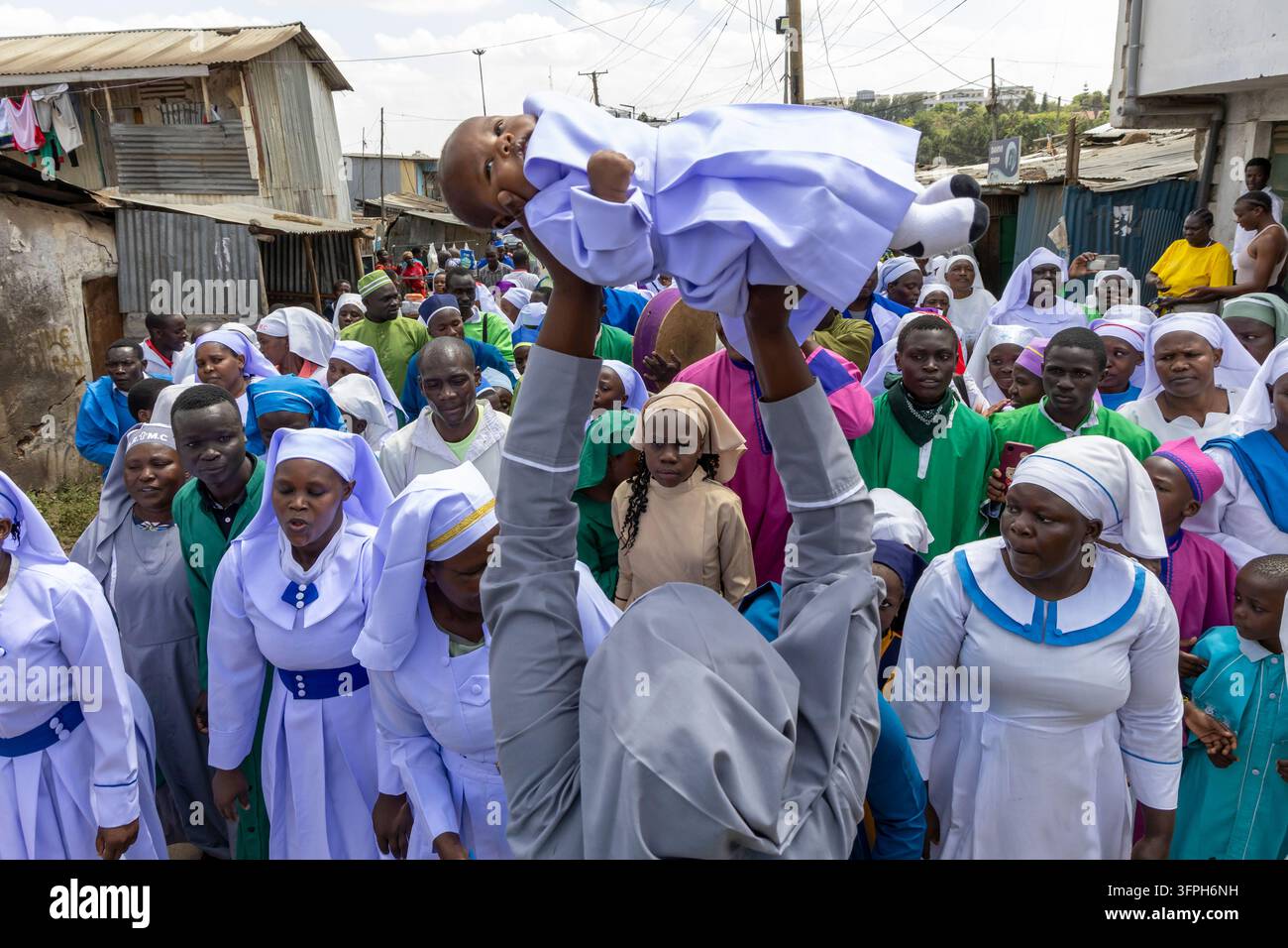 Persona che solleva un bambino in un abito lilla sopra una folla di fedeli durante una processione battesimale a Kibera, Contea di Nairobi, Nairobi, Kenya Foto Stock